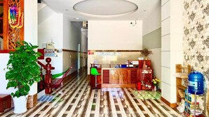 A hotel lobby with a patterned floor, a reception desk, a green chair, and a potted plant. - Chan Hotel Phu Quy (Phu Quy)