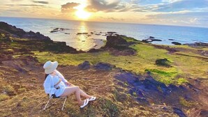 A person sitting on a chair overlooking a coastal landscape with the sun setting over the water. - Chan Hotel Phu Quy (Phu Quy)