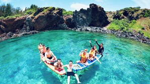 A group of people on a paddleboard in a clear, shallow water body surrounded by rocky terrain and greenery. - Chan Hotel Phu Quy (Phu Quy)
