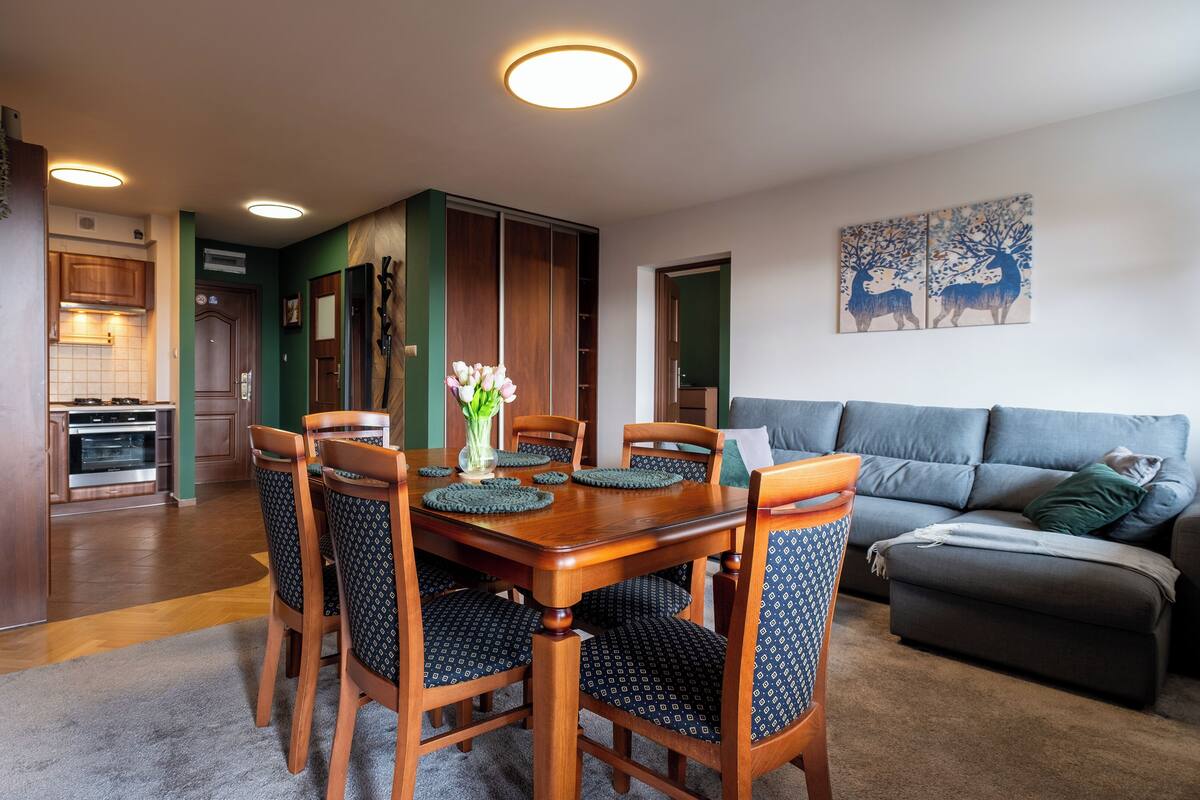 Un coin repas avec une table et des chaises en bois, un vase rempli de fleurs et, au fond, un canapé gris.