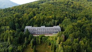 Et hotel med flere etager og fladt tag, omgivet af tæt skov og bjerge i baggrunden.