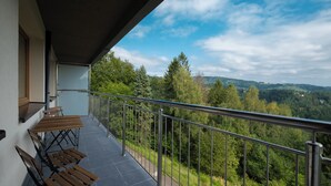 En balkon med udsigt over en skovdal og fjerne bakker.