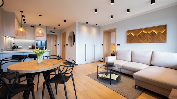 En moderne stue med et rundt træspisebord, sorte stole, en beige sofa og et glasbord.
