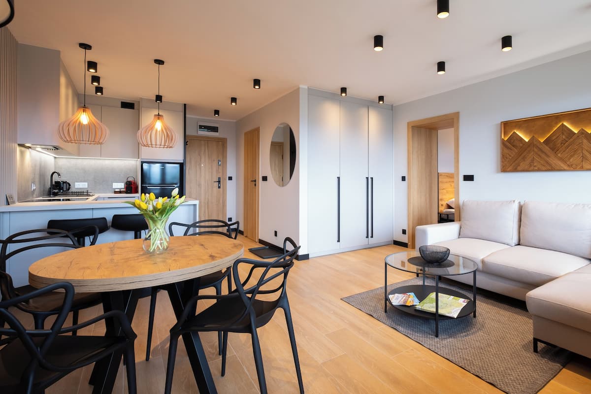 Un salon moderne avec une table de salle à manger ronde en bois, des chaises noires, un canapé beige et une table basse en verre.