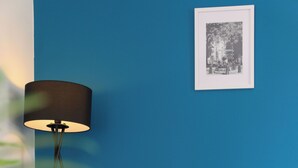A room with a teal-colored wall, a framed black and white photo, a black floor lamp, and a plant with green leaves.