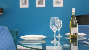 A dining table with a wine bottle, two glasses, and plates set for a meal.