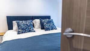 Een net opgemaakt bed met een blauw-wit gestreept hoofdeinde, een wit kussen en een blauwe deken.