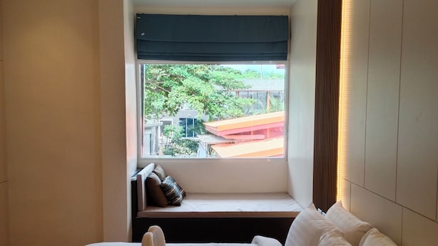 A hotel room with a large bed, a window seat with a view of buildings and greenery, and a modern design. - Tommy Resort2 (Ko Pha-ngan)