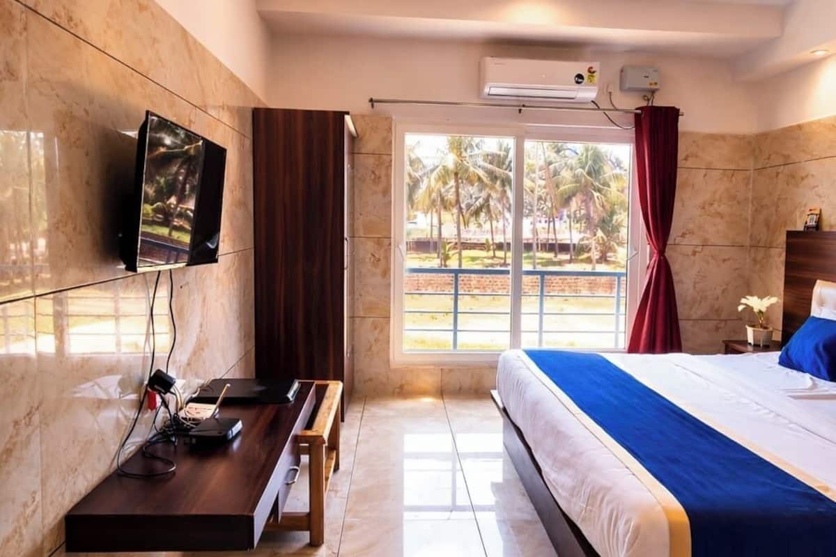 Habitación de hotel con cama, escritorio, televisión, ventana con vista a palmeras y un equipo de aire acondicionado.