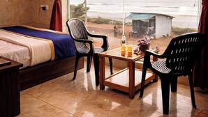 Una habitación con una cama, una mesa con bebidas, dos sillas y un ventanal con vistas a la playa.