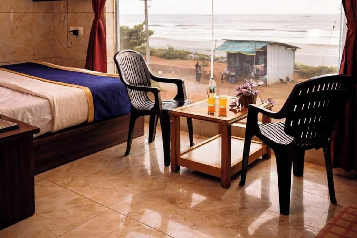 Una habitación con una cama, una mesa con bebidas, dos sillas y un ventanal con vistas a la playa.