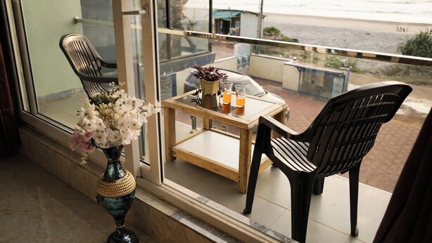 Un balcón con una mesa, sillas, un florero con flores y vista a la playa.