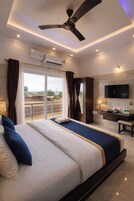 Habitación de hotel con una cama grande, ventilador de techo, aire acondicionado, televisión y vistas al exterior.