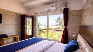 Habitación de hotel con cama, una mesita, televisor y ventana con vista a la playa y palmeras.