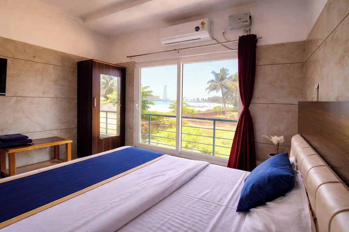 Habitación de hotel con cama, una mesita, televisor y ventana con vista a la playa y palmeras.