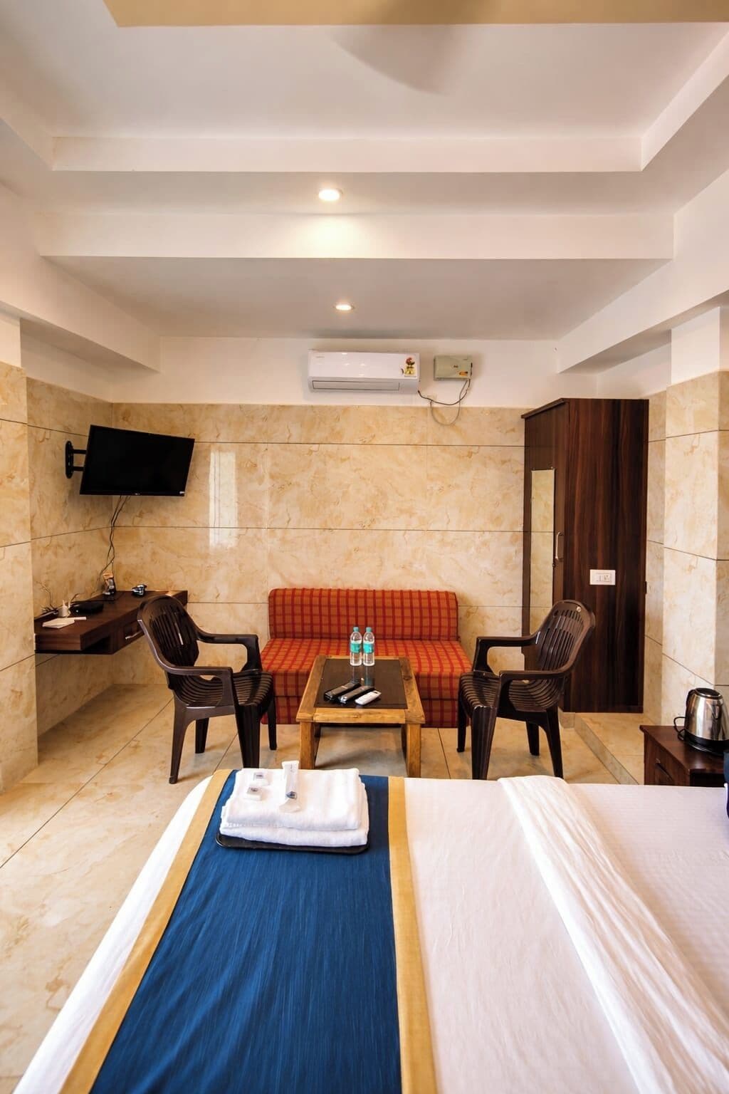 A hotel room with a bed, a sofa, a TV, a desk, and an air conditioning unit.