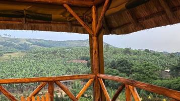 Una mesa y sillas de madera bajo un tejado de paja, con vistas a un paisaje exuberante.