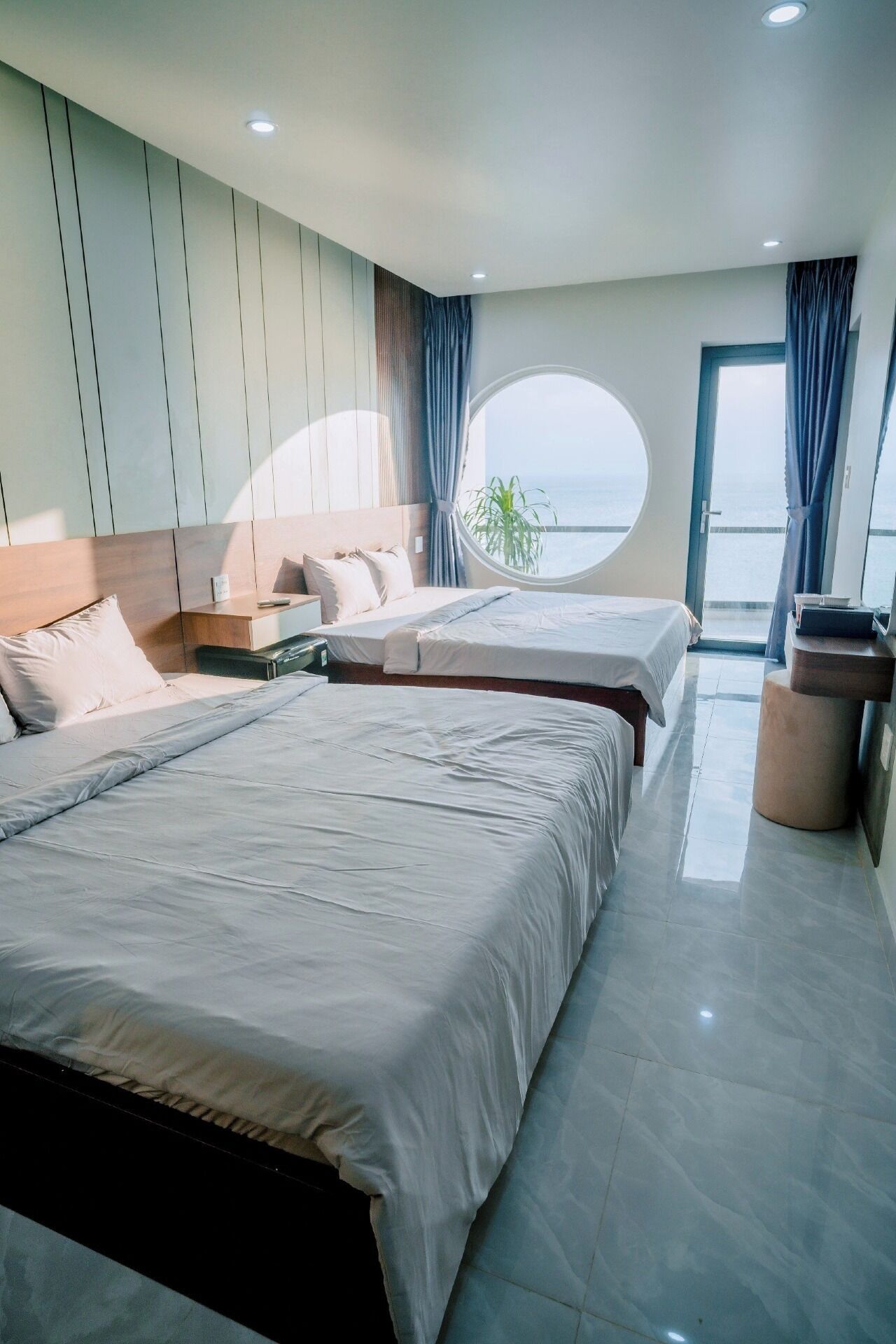 Une chambre moderne avec deux lits, une fenêtre ronde et une vue sur la mer.