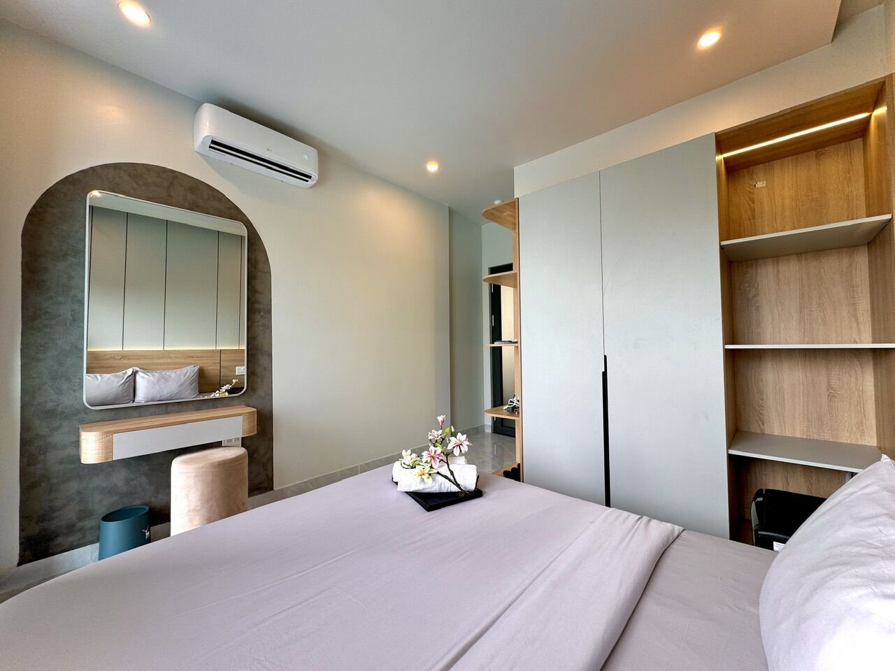 Een moderne hotelkamer met een groot bed, een inbouwkleerkast, een kaptafel met spiegel en een klein badgedeelte.