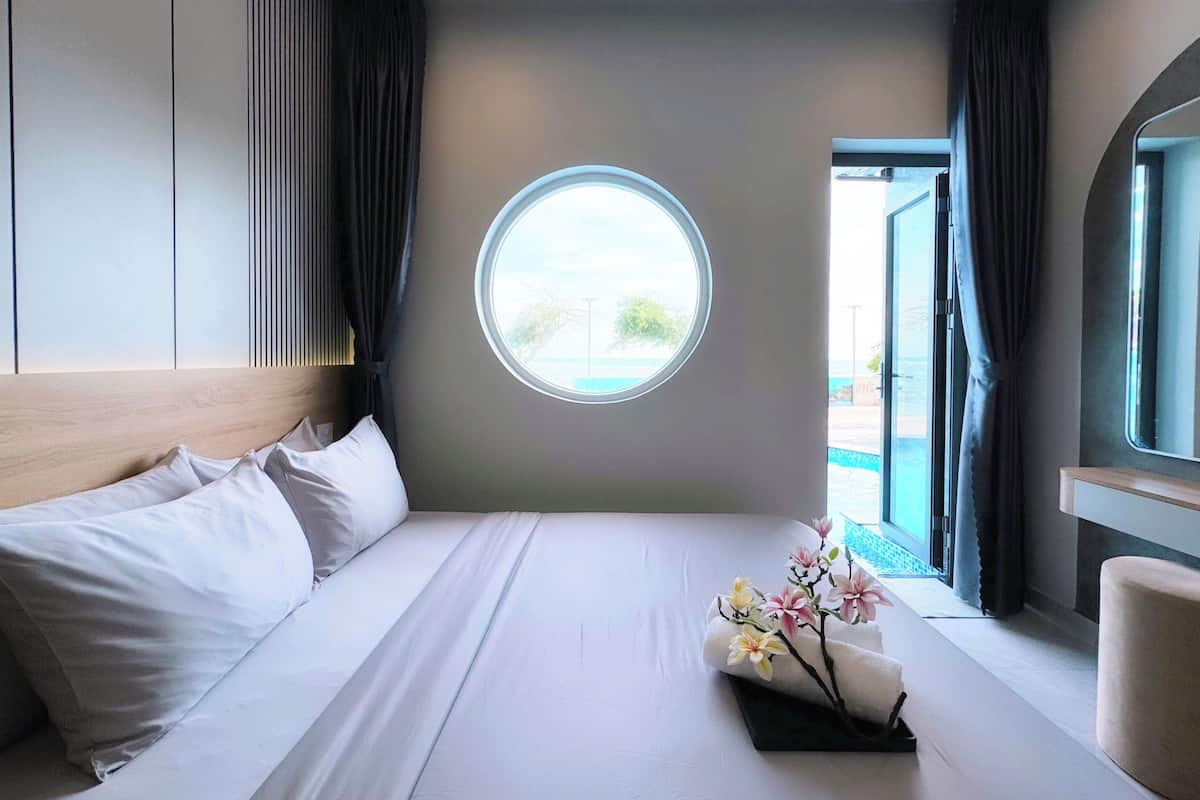 Una habitación de hotel moderna con una cama grande, un ventanal redondo y vistas al exterior.