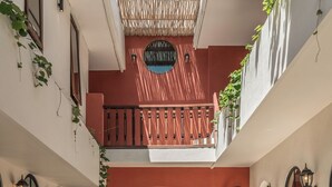 A courtyard with a central water feature, wooden doors, and a balcony with plants. - Casa Galicia (Canggu)