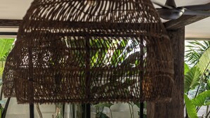 A modern interior with a woven ceiling structure, a wooden table with a decorative item, and green cushioned seating. - Casa Galicia (Canggu)