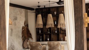A room with a wooden ceiling, a stone wall, and a bar area with wicker chairs and a wooden table. - Casa Galicia (Canggu)