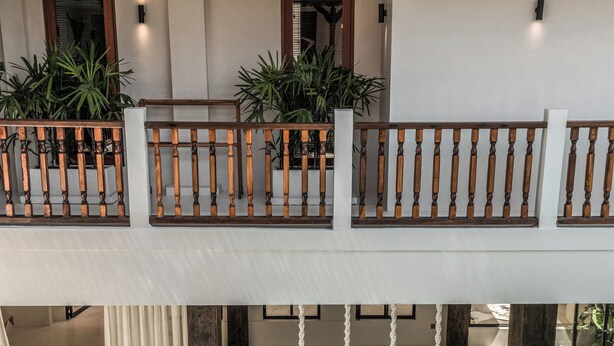 A two-story building with a pool on the ground floor and a balcony with wooden railings and potted plants. - Casa Galicia (Canggu)