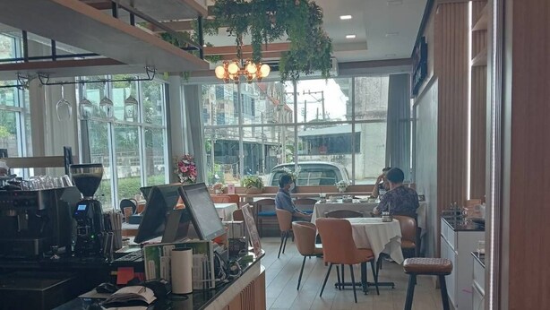 A modern cafe with a wooden counter, seating area, and large windows. - Wellness World Chiva 89 (Bangkok)