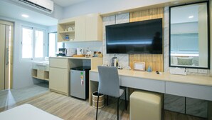 A modern kitchen with a built-in refrigerator, microwave, and stove. There is a large flat-screen TV mounted on the wall, a small trash bin, and a chair. - Wellness World Chiva 89 (Bangkok)