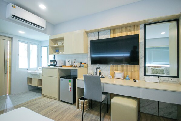 A modern kitchen with a built-in refrigerator, microwave, and stove. There is a large flat-screen TV mounted on the wall, a small trash bin, and a chair. - Wellness World Chiva 89 (Bangkok)