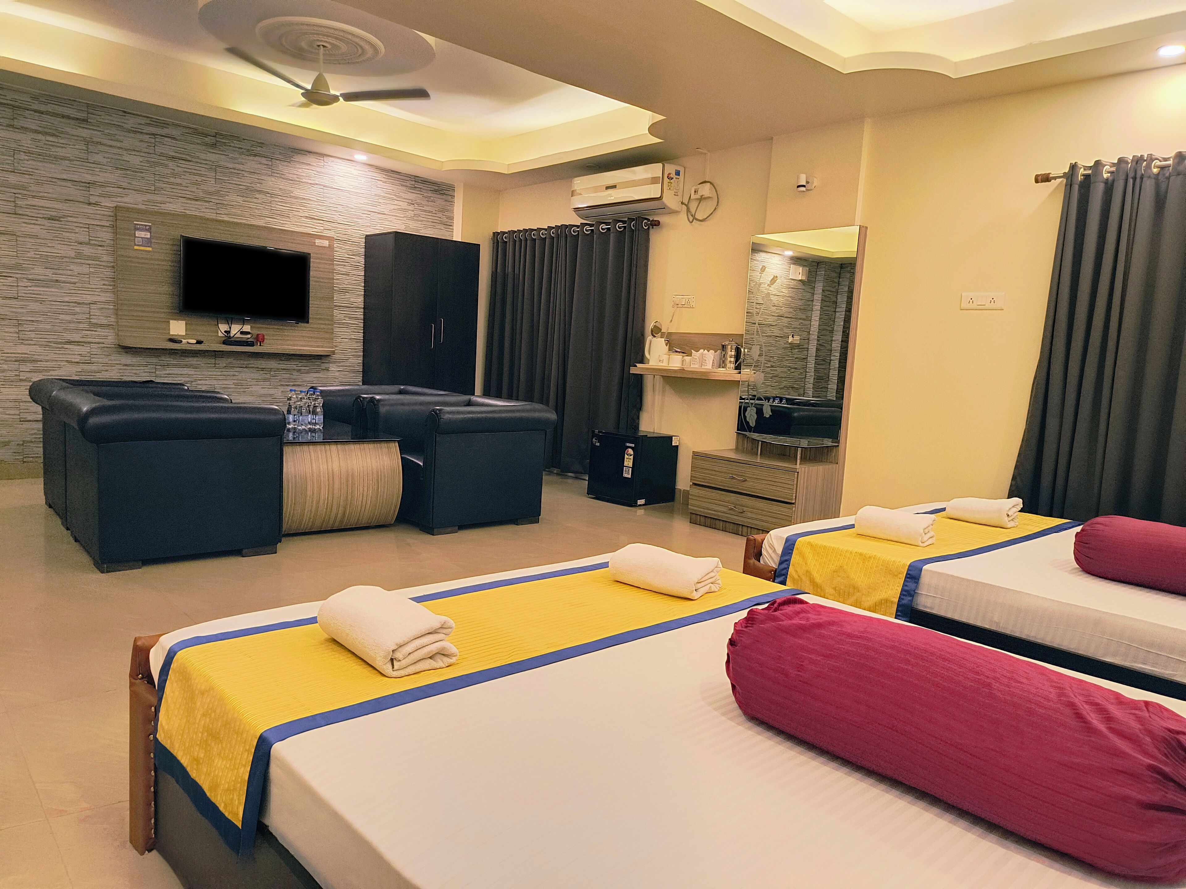 A hotel room with two beds, a sofa, a TV, and a minibar.
