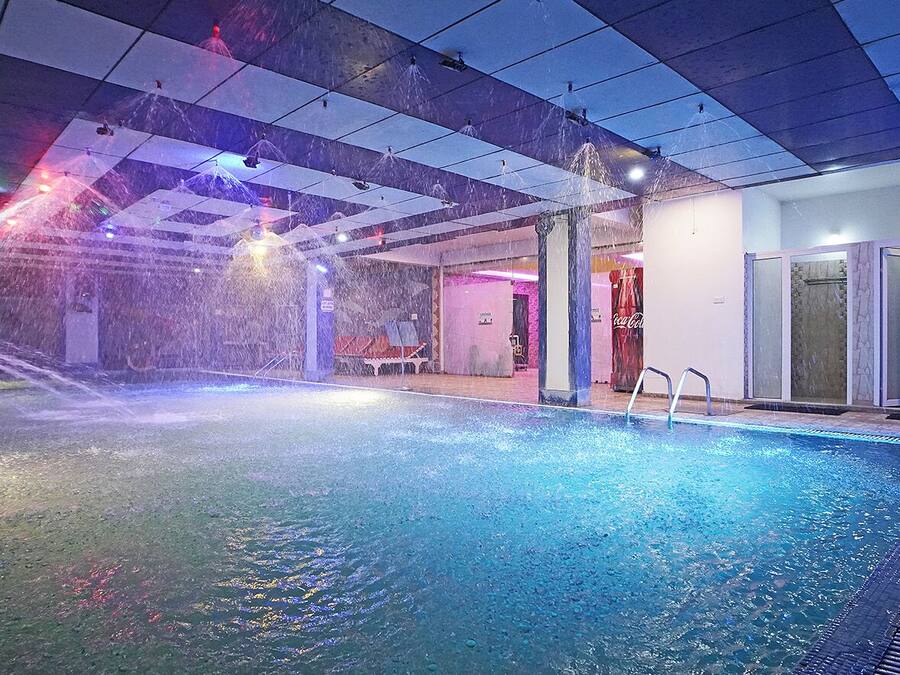 An indoor swimming pool with water jets, a Coca-Cola sign, and a glass door entrance.