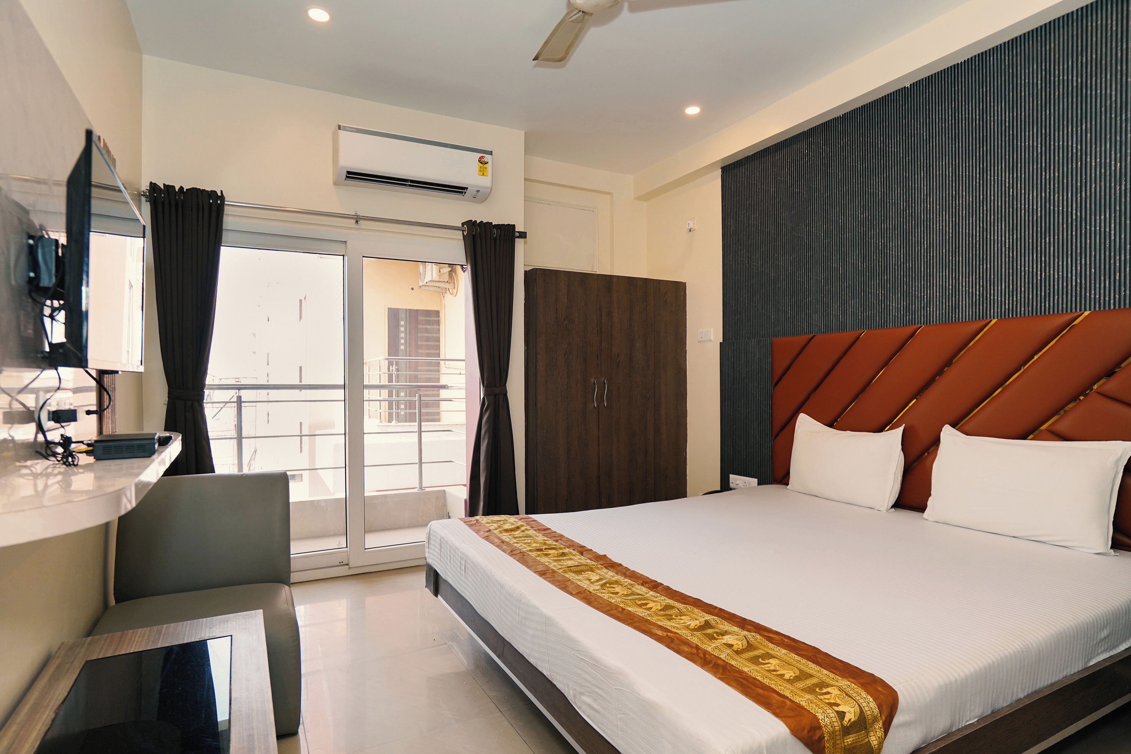 A hotel room with a large bed, a desk, an air conditioning unit, and a view of the outside.