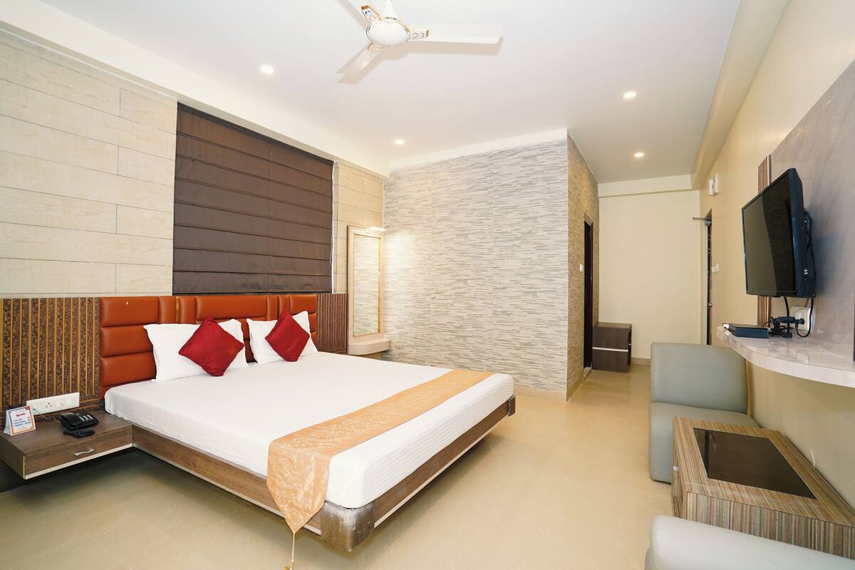 Una habitación de hotel moderna con una cama grande, un televisor de pantalla plana montado en la pared, un pequeño rincón de estar y un ventilador de techo.