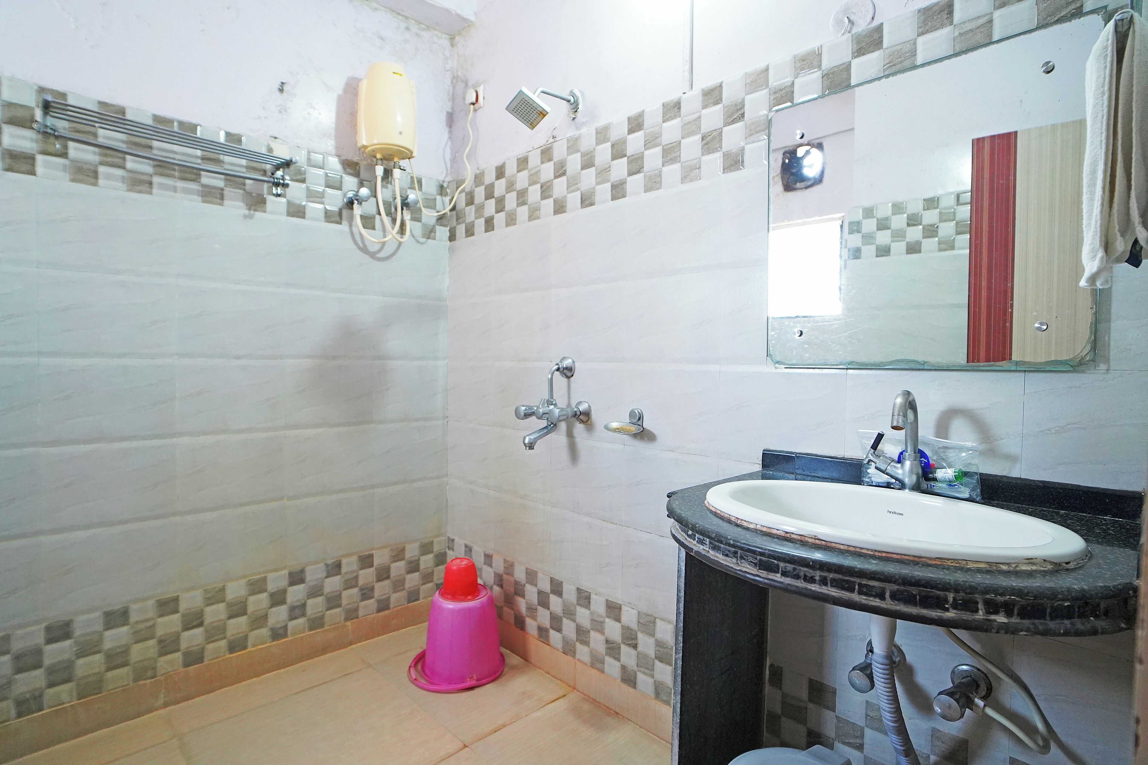 A bathroom with a tiled floor, a sink with a mirror above it, a showerhead, and a toilet.