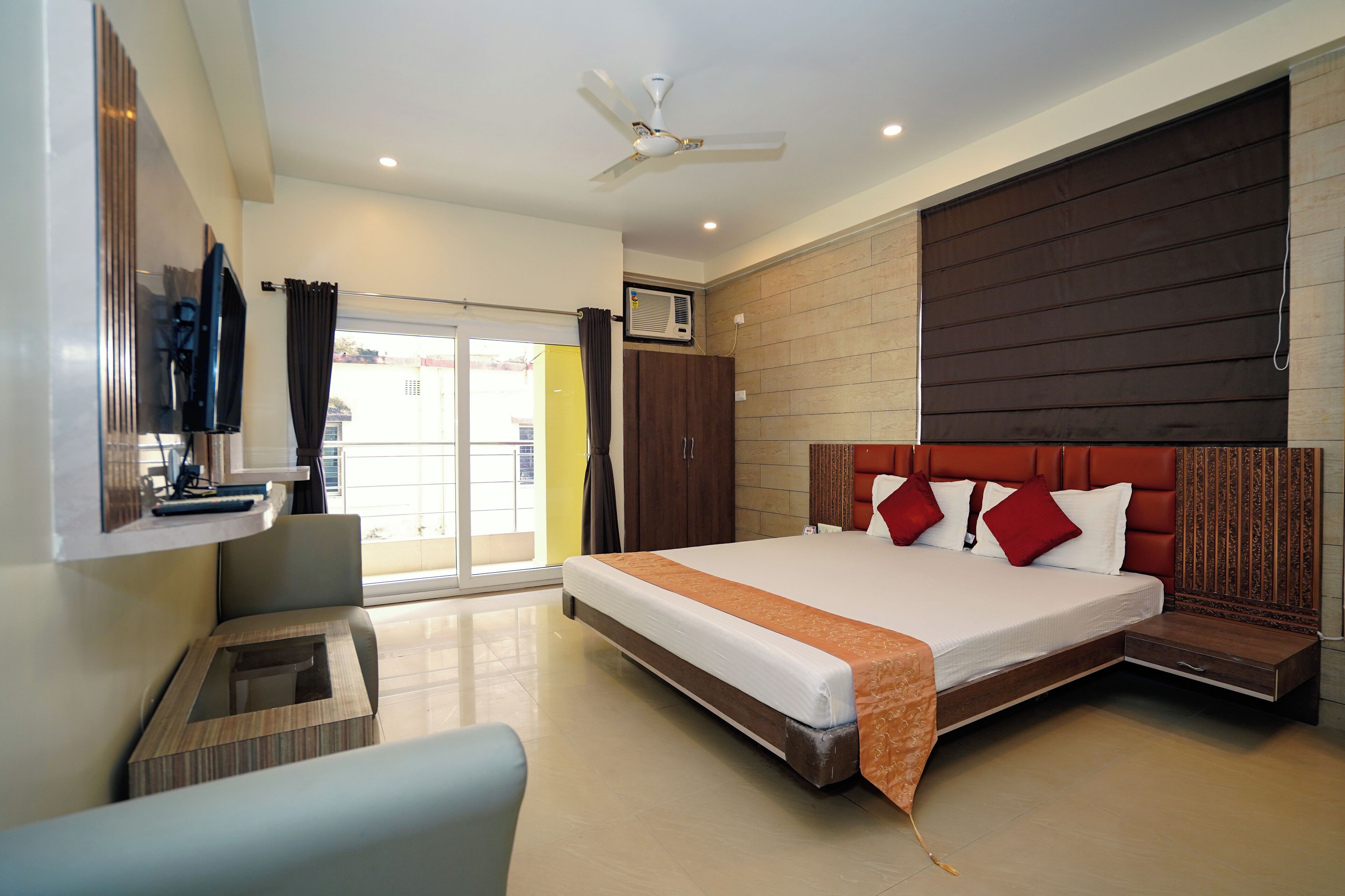 A hotel room with a large bed, a ceiling fan, a TV, and a sliding glass door leading to a balcony.
