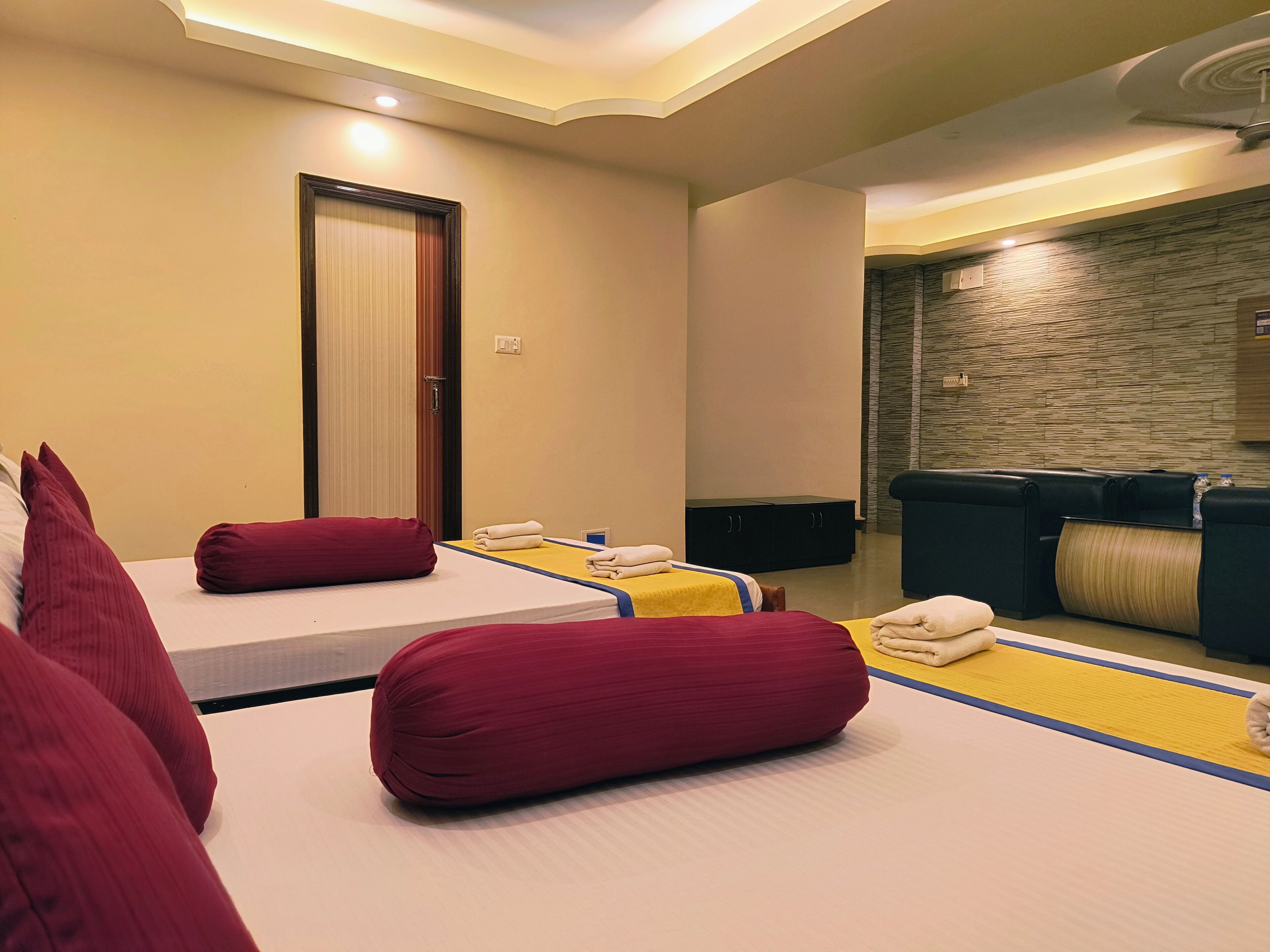 A hotel room with two beds, a sofa, and a stone wall.