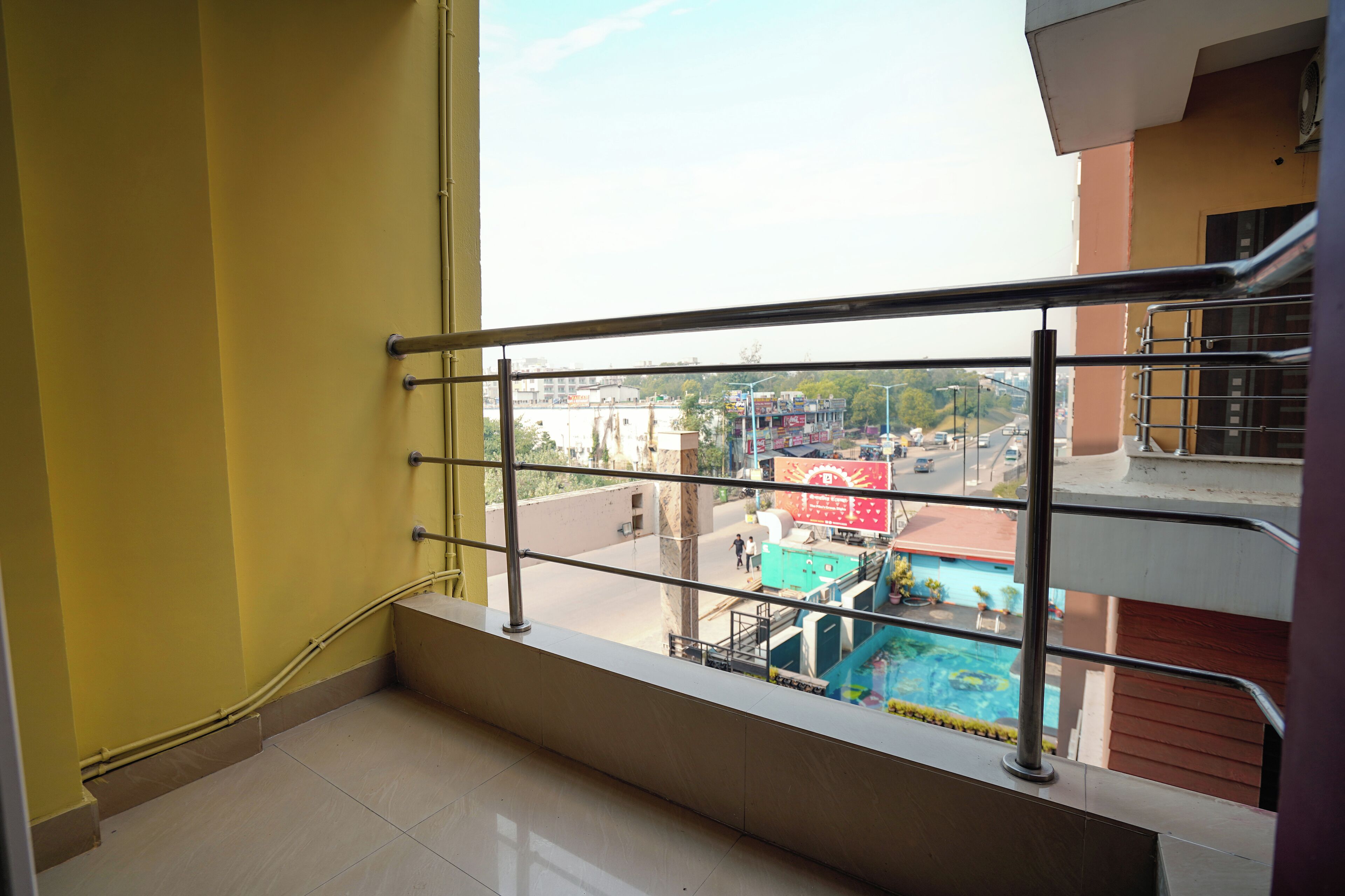 A balcony with a metal railing overlooking a swimming pool and buildings.
