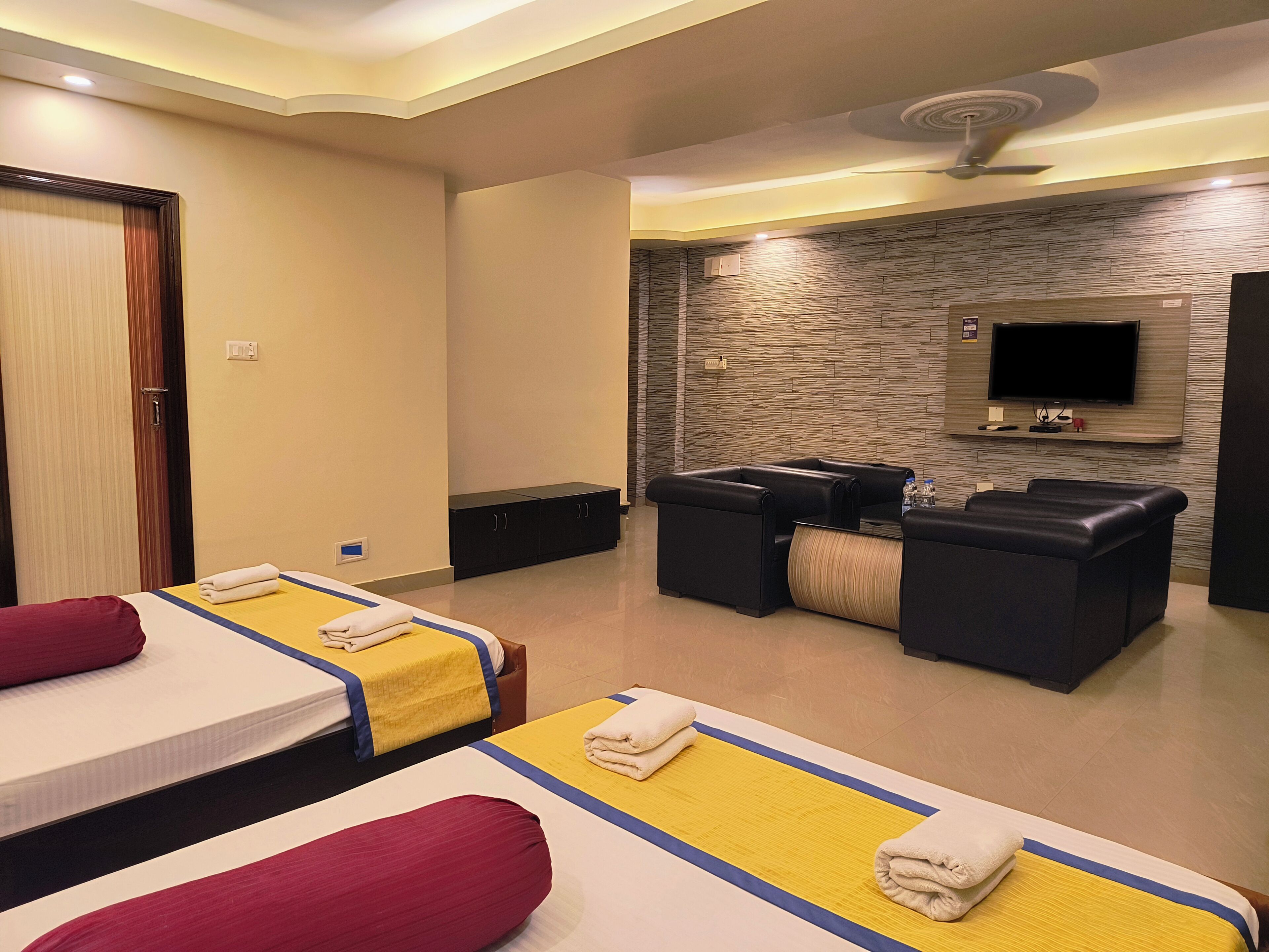 A hotel room with two beds, a massage table, a TV, and a stone wall.