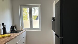 Una cocina con un refrigerador negro, encimera de madera, armarios blancos y una ventana con vista a árboles.