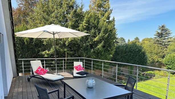 Una terraza con una mesa, sillas, un parasol grande y una barandilla.
