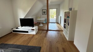 Una sala de estar moderna con un televisor de pantalla plana sobre un soporte blanco, una mesita redonda con sillas y una estantería.