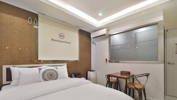 A hotel room with a bed, a small table with chairs, an air conditioning unit, and a window with a frosted glass.