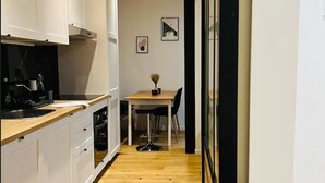 A narrow kitchen with white cabinets, a wooden countertop, and a dining area with a table and chairs. - Apartment Paris 11 - 2 bedrooms - 2 shower rooms - 2 toilets (Paris)