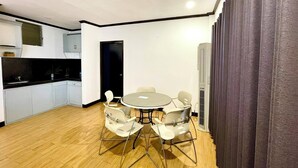 Una cocina compacta con armarios blancos y encimera negra, una mesa redonda con cuatro sillas, y una puerta de color oscuro.