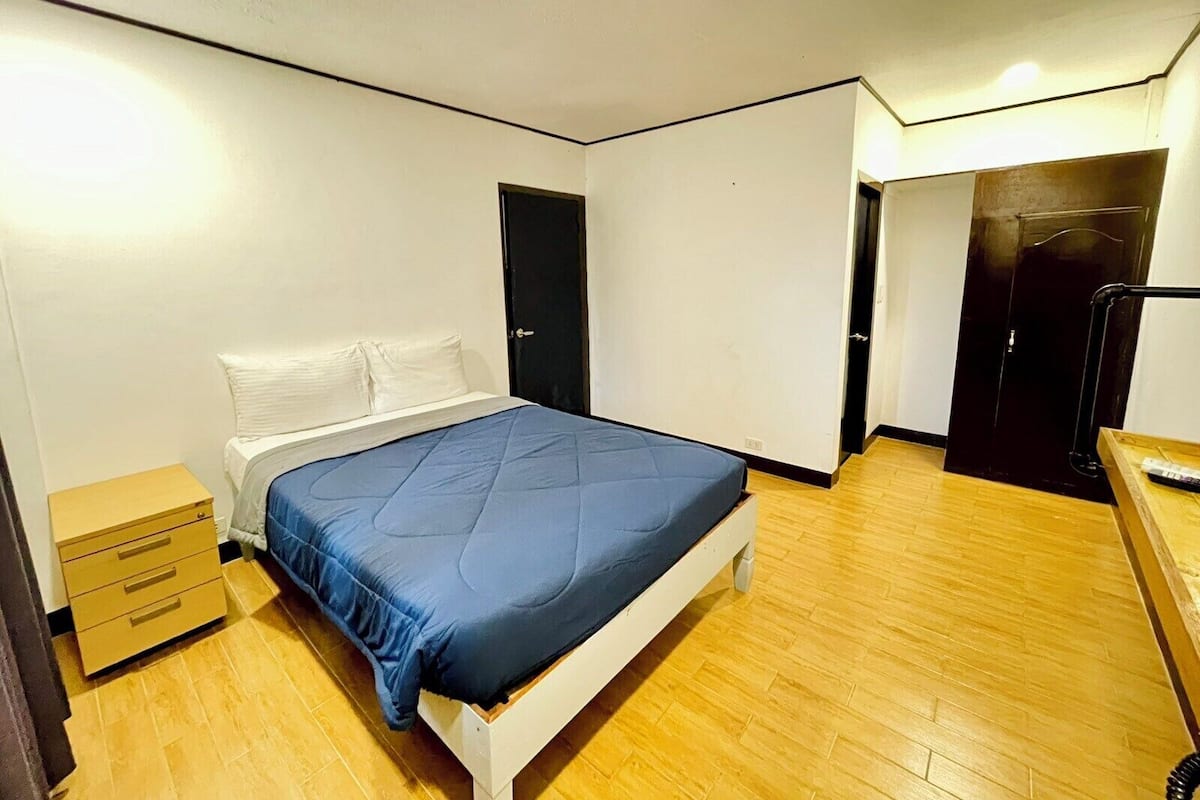 Quarto com uma cama, penteadeira de madeira e uma porta.