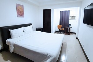 A hotel room with a large bed, a desk with a chair, a television, and a door leading to another room. - Bluewing Hotel Angeles powered by Cocotel (Angeles City)