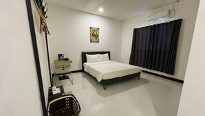 Habitación de hotel con cama, escritorio con silla, aire acondicionado de pared y ventana con cortinas, además de un cartel en la pared.