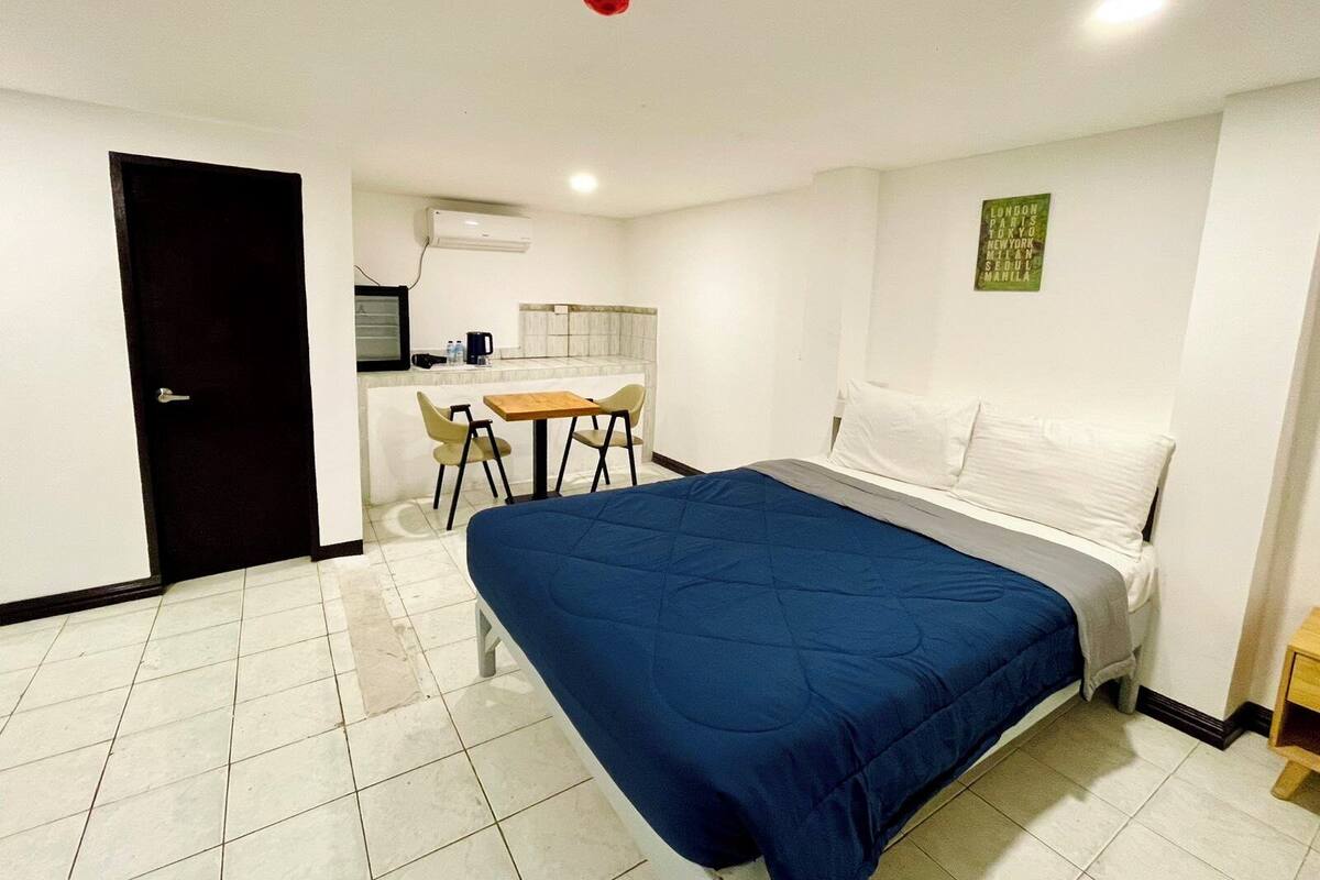 Quarto de hotel com cama, uma pequena mesa com cadeiras, cozinha compacta e porta.
